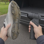 Oryn Original clearing loose grass from a supported golf shoe beside an open car trunk.